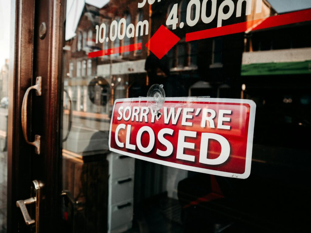 Close-up of a shop's closed sign on a glass door reflecting the street outside.