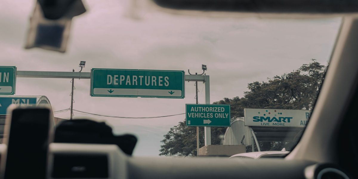 View through windshield of car driving towards airport departure signs and authorized vehicle only lane, captured in soft daylight.